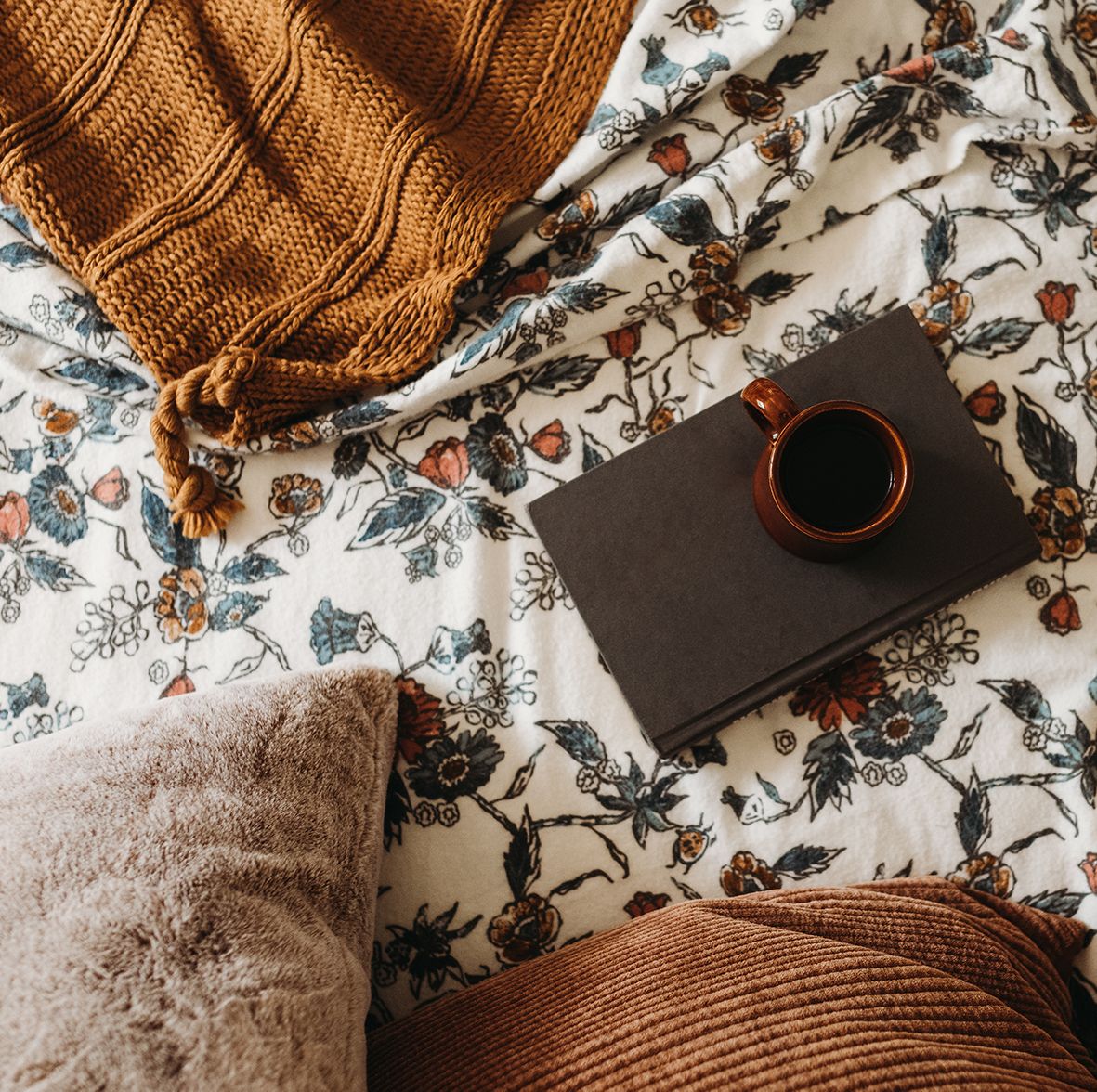 coffee and book on top of floral print flannel sheets