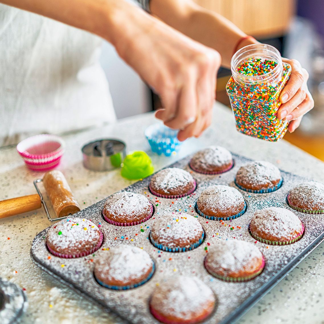 baker adding sprinkles to cupcakes