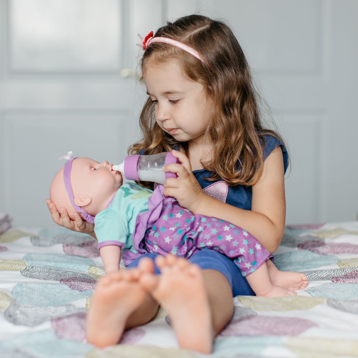 young girl feeding bottle to baby doll on bed