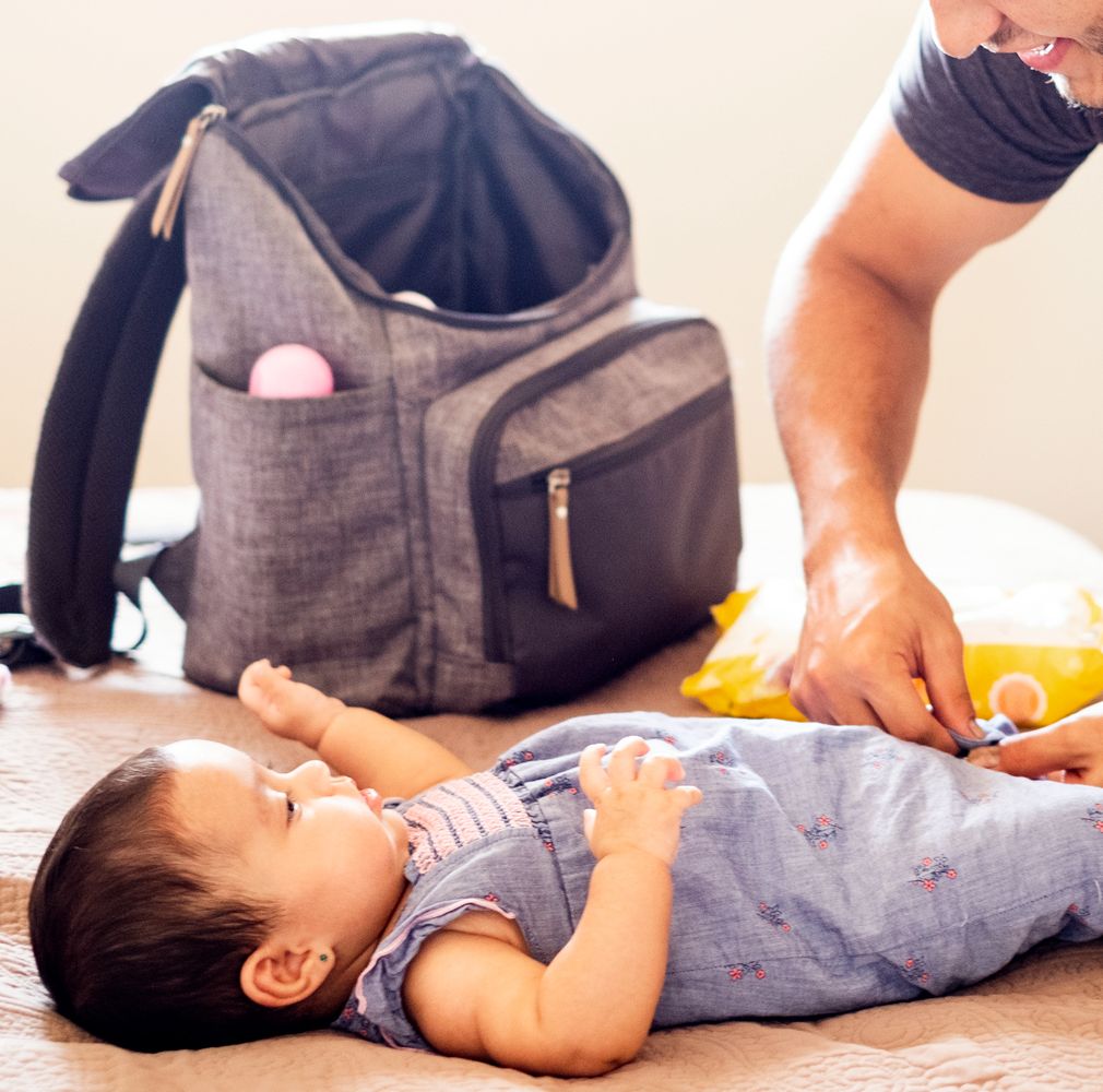 dad changing baby with diaper backpack on bed