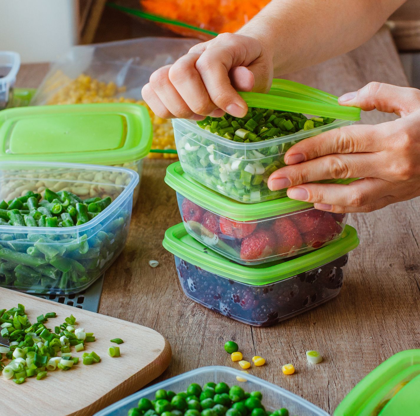 close up of woman preparing plastic food boxes with fresh green onion, strawberry and blackberry for freezing on the wooden table