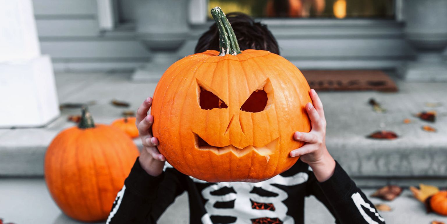 kid in skeleton costume holding up jack o lantern carved pumpkin