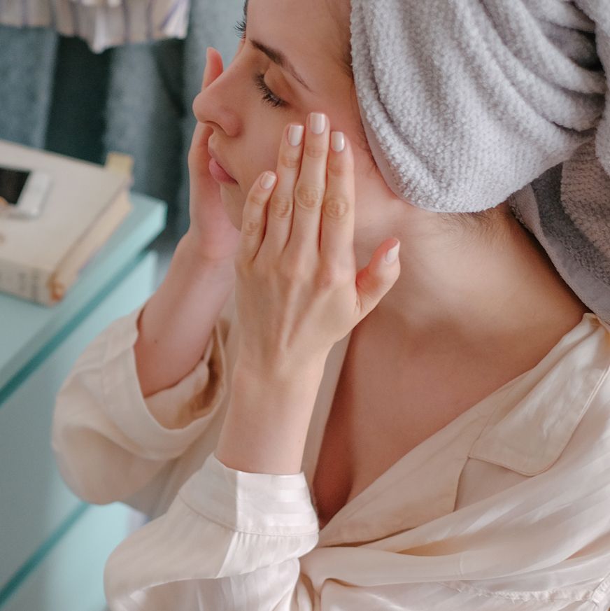 woman in towel doing skincare routine in mirror