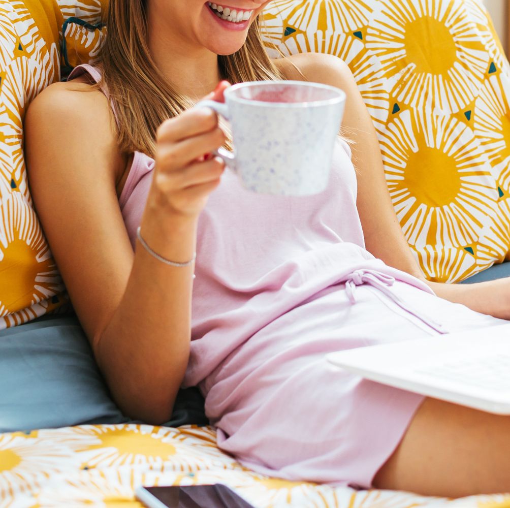 woman laying in bed with laptop and coffee mug in pajamas